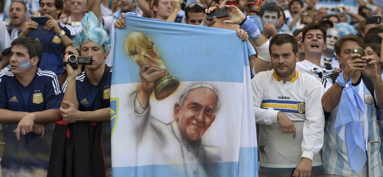 Papa Francesco alza la Coppa del Mondo: il disegno sulla bandiera argentina accende lo show sugli spalti della partita con l&#39;Iran a Belo Horizonte. Afp